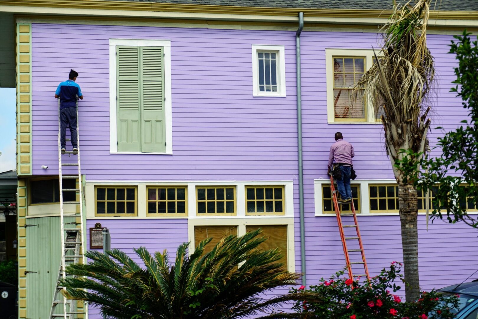 A man on a ladder painting the side of a house.